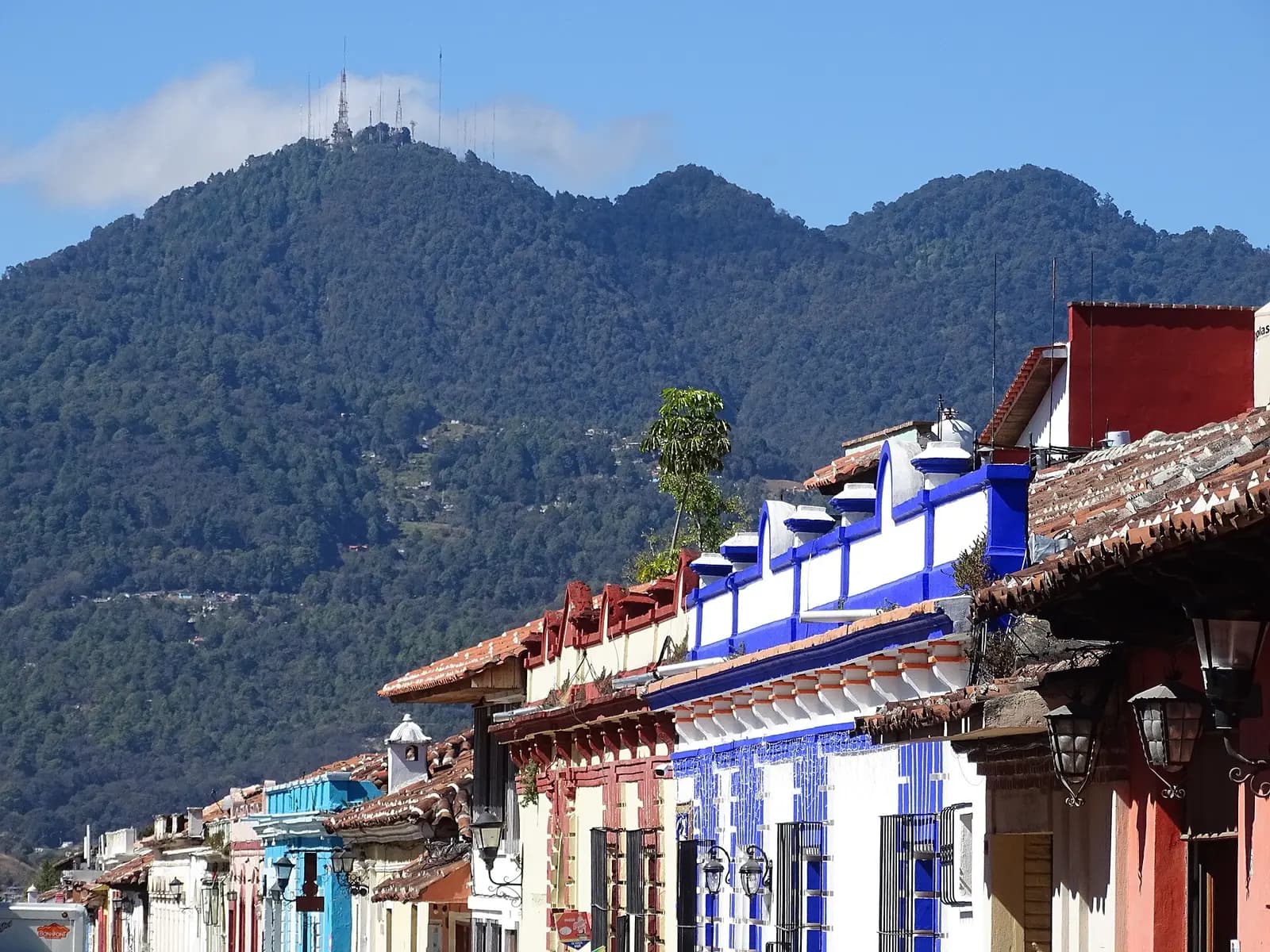Tejados coloridos y fachadas coloniales de San Cristóbal de las Casas con una montaña boscosa al fondo.